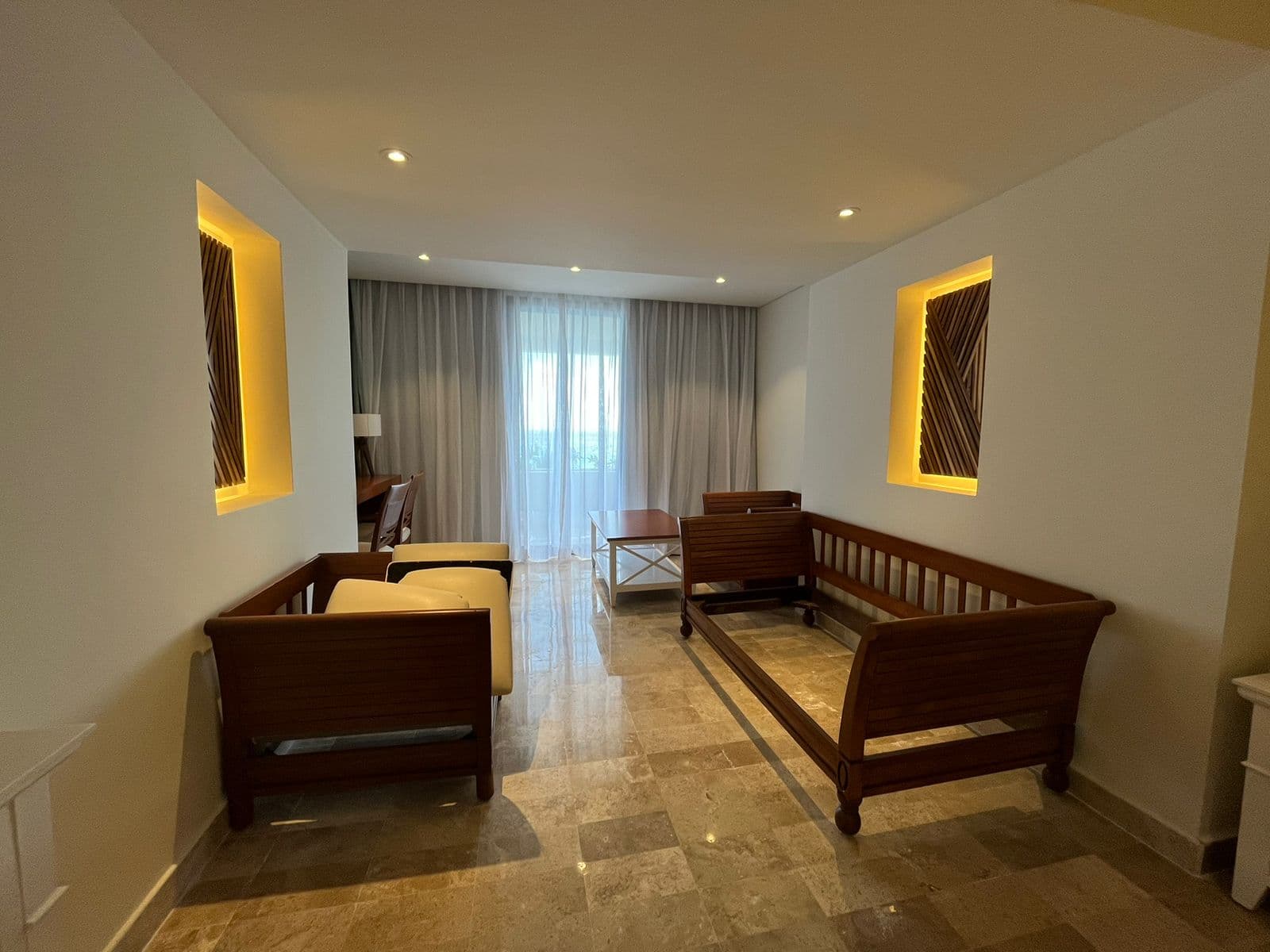 Área de sala en habitación — mobiliario de madera, acentos de panel retroiluminado, piso de travertino